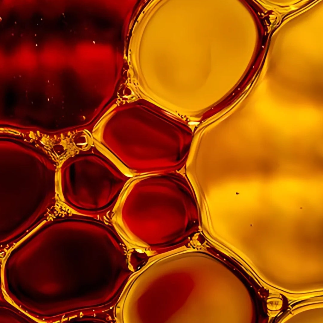 A clear glass filled with oil and water, showcasing colorful red and yellow bubbles suspended in the mixture.